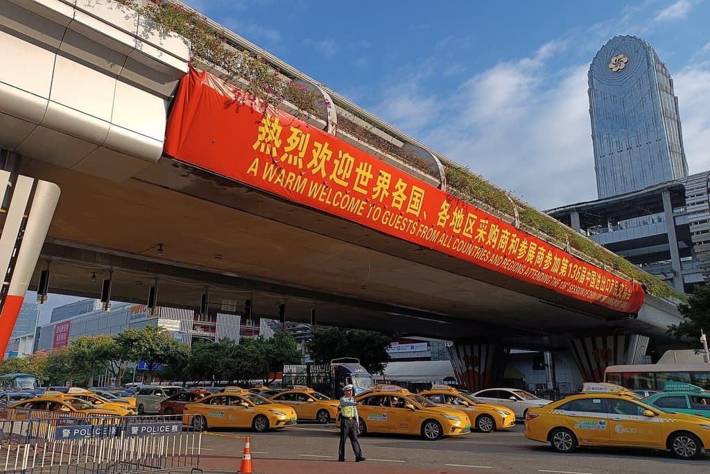 A red banner across a footbridge at Pazhou welcoming buyers from all over the world to the 136th Canton Fair, taxis queuing below